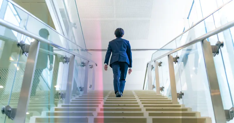 A professional walking up the stairs in a modern office building, symbolizing career growth and new job opportunities