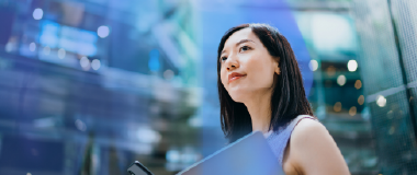 Confident young professional woman holding a laptop and looking ahead in a modern city environment
