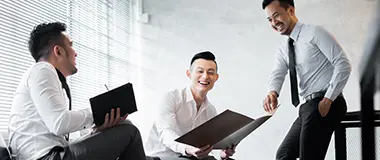 Three businessmen in shirts having a discussion and smiling in an office
