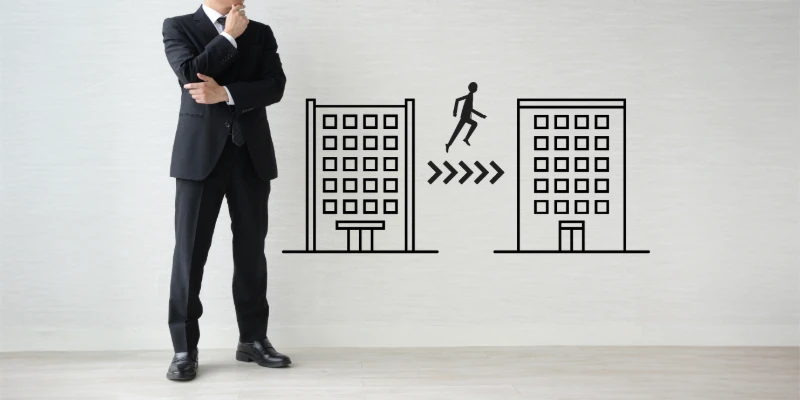 A businessman standing between two illustrated office buildings, thinking about job change.