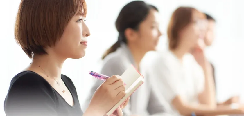 ノートにメモを取る女性と学習中の人々