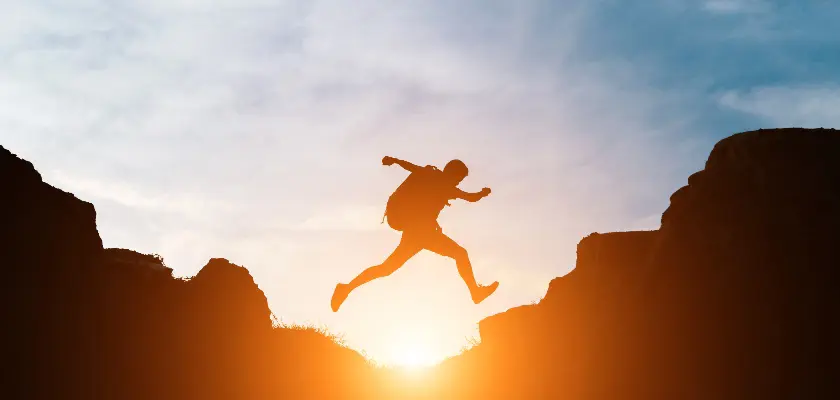 Silhouette of a man jumping across cliffs at sunset