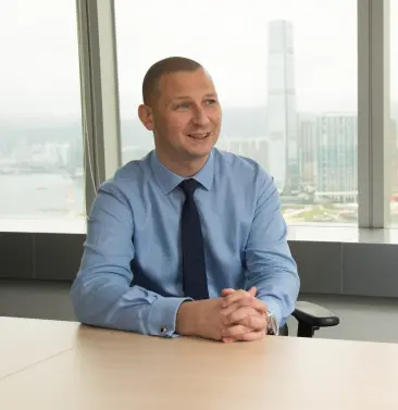 Businessman in a blue shirt sitting at a desk and smiling with city skyline in the background