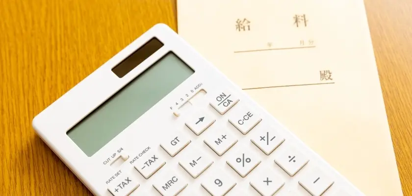 電卓と給料明細 木製のテーブルに置かれた白い電卓と給料明細書。電卓のディスプレイと数字ボタンが見える。
