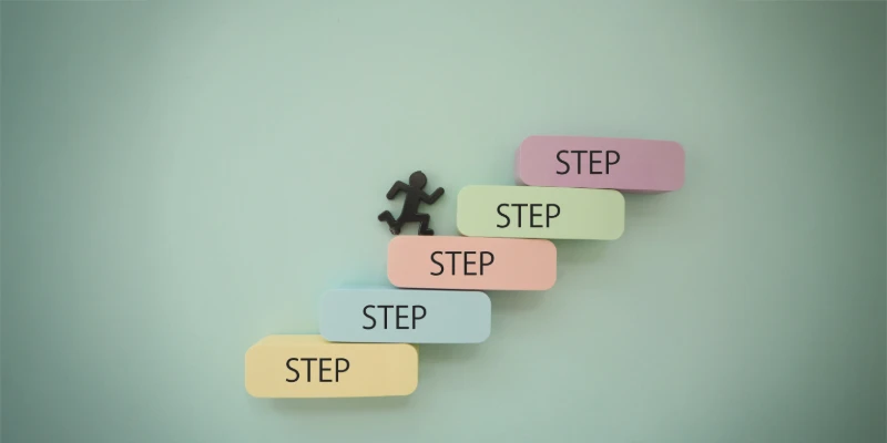 「STEP」と書かれたカラフルな階段を登る小さな人のシルエット。
