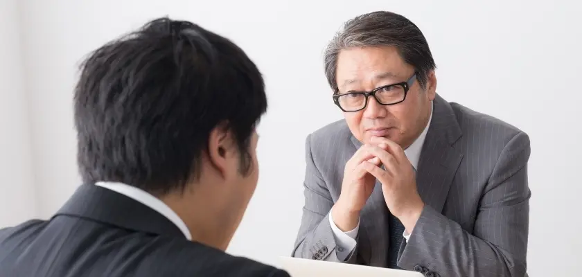面接官に真剣な表情で話を聞かれるスーツ姿の男性