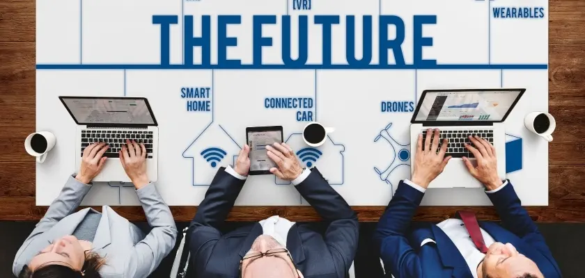 未来のテクノロジー会議 「THE FUTURE」と書かれた大きなポスターを囲んで作業する4人のビジネスパーソンの俯瞰図。ポスターには「SMART HOME」「CONNECTED CAR」「DRONES」「WEARABLES」などの未来技術が描かれている。