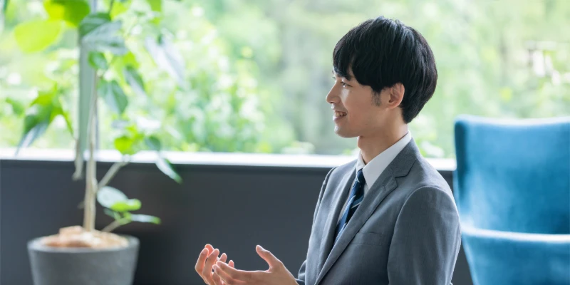 A man in a gray suit speaking positively during an interview in a bright office.