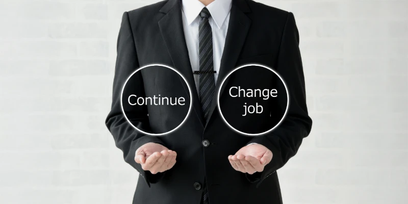 「Continue」と「Change job」と書かれた円を両手に持つビジネスマン。キャリアの選択を象徴。